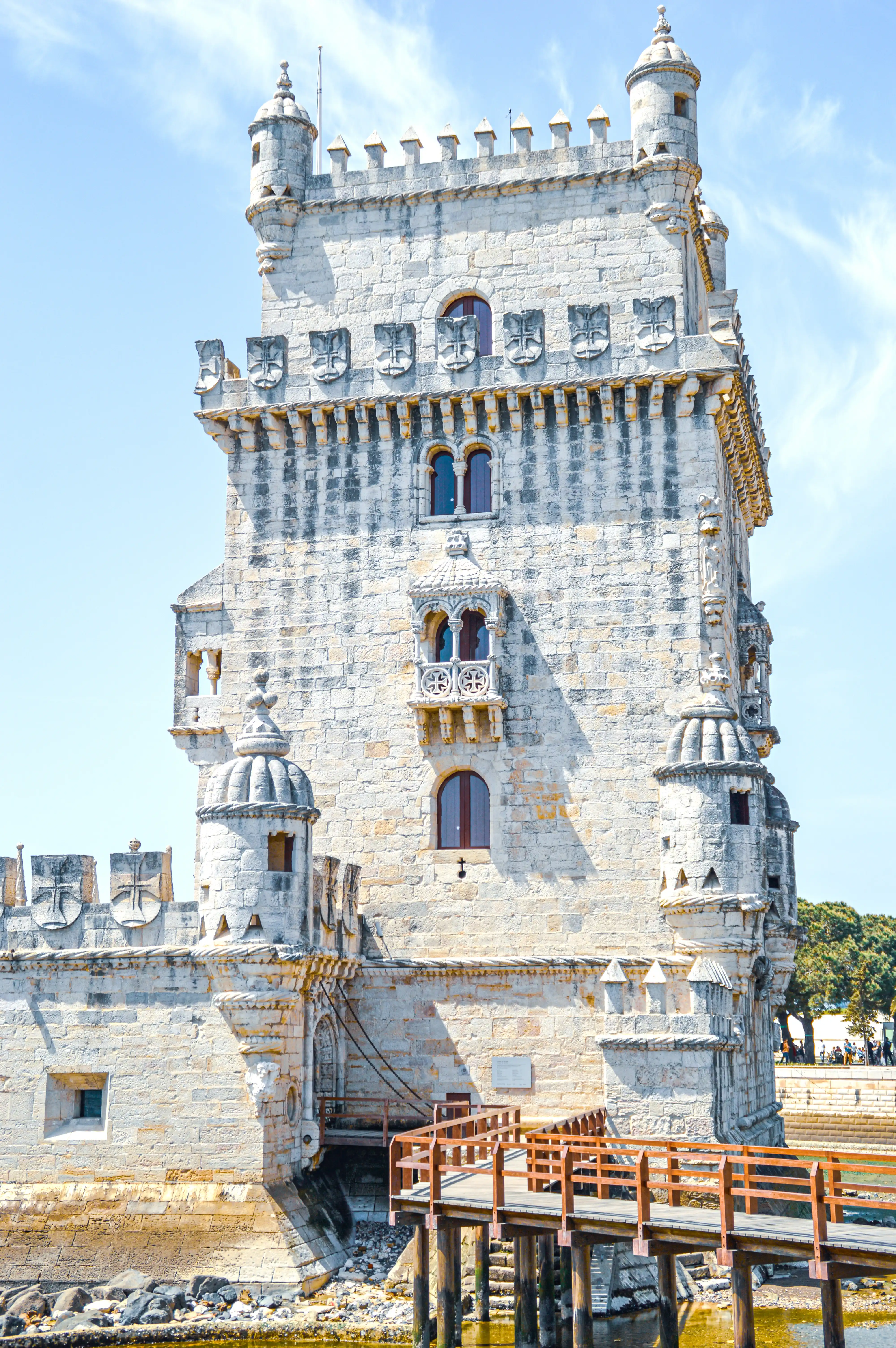 Front view of the historic Belém Tower in Lisbon, Portugal, a stone fortification with ornate details, accessed by a wooden bridge over water.